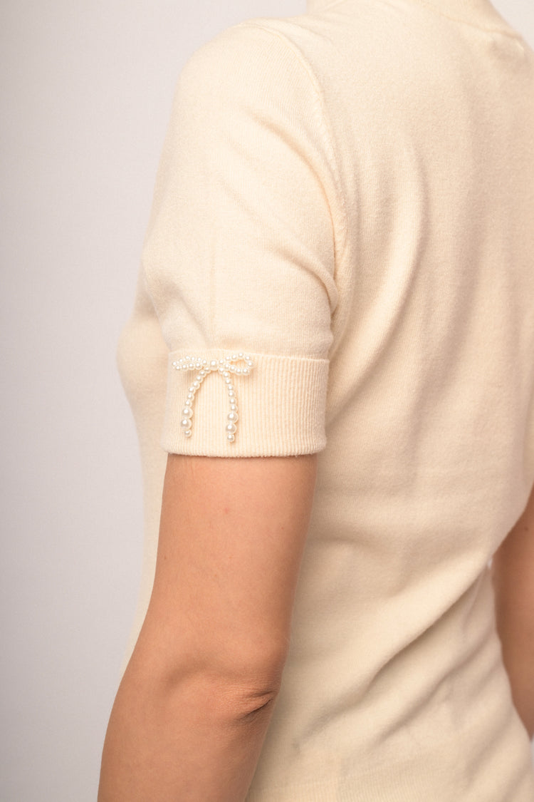 Lupetto in maglia beige con fiocchetti decorativi alle mezze maniche